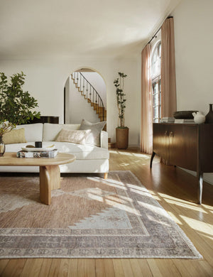 The Kate desert palette geometric floor rug sits in a living room with a white linen sofa, natural wooden coffee table with sculptural legs, and a wooden anabella console table.