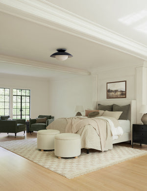  Two Kamila White Boucle 24-inch ottomans sit at the end of a ivory linen framed bed with olive linens atop a checkerboard rug