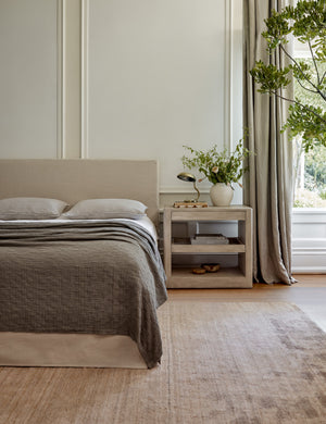 The Chiltern mauve rug lays in a bright bedroom under a natural linen framed bed and a light wooden night stand