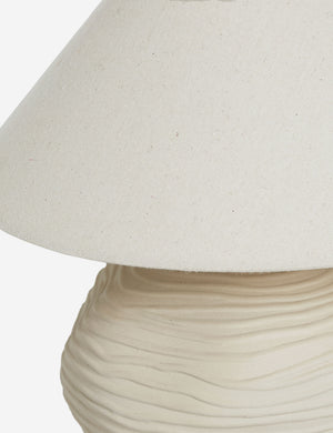 Close-up of the Wrinkle Table Lamp by Sarah Sherman Samuel, featuring a textured beige ceramic base with wavy details and a wide, plain fabric shade against a white background.