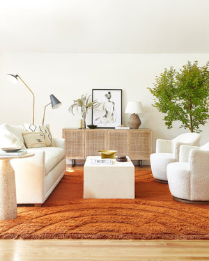 The Annika dual arm floor lamp with black marble base and black finish sits in a living room with two boucle swivel chairs, a woven sideboard, and a terracotta colored rug