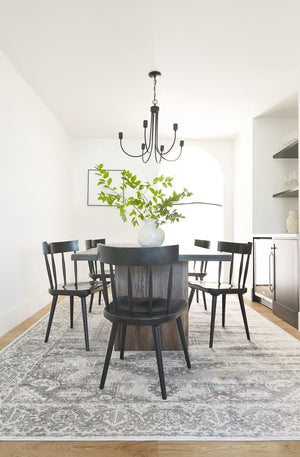 Five Neema black mahogany dining chairs surround a dark wooden dining table, all sitting atop a gray and black persian rug.