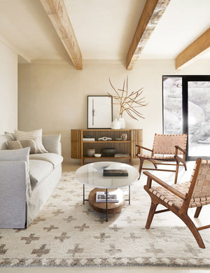 Two Jaslene beige woven leather accent chairs sit in a living room across from a gray linen sofa and white oval coffee table