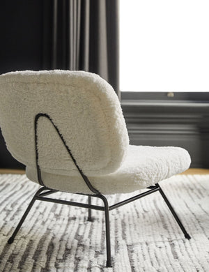 Rear view of the Amanda white plush upholstered accent chair that sits on a white and gray textured rug in a black painted room.