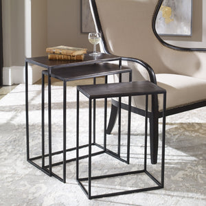 The Loletta black nesting tables are partially nested under each other, sitting in a living room next to a black wooden framed accent chair atop a gray patterned rug