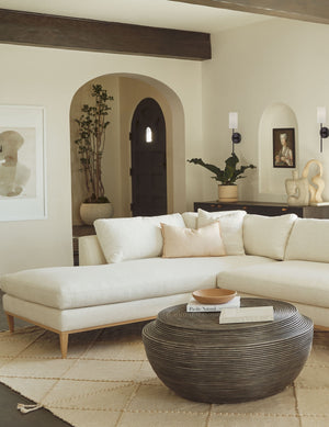 The Sina gray washed handcrafted paper mache vase sits in the corner of a living room with a white sectional sofa, a round wooden coffee table, and a natural textured rug