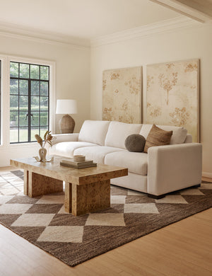 The Brisa rectangular burl wood coffee table with four legs sits in a classic living room with an ivory sofa and a brown and cream diamond-patterned rug.