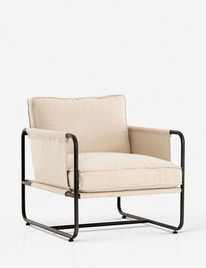 Angled view of the Alena accent chair with cream linen cushions and black metal frame