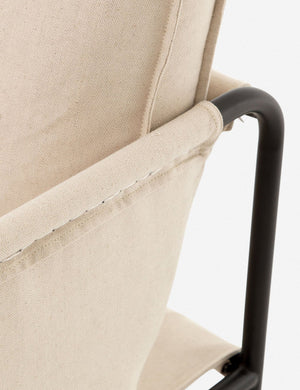 Close-up of the arm and black metal base from the outside of the Alena accent chair with cream linen cushions