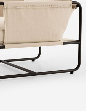 Close-up of the arm and black metal base from the outside of the Alena accent chair with cream linen cushions