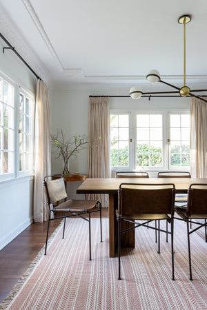 The Adeline black and brass retro chandelier sits in a dining room with velvet dining chairs, a rectangular dark oak dining table, and a red patterned rug