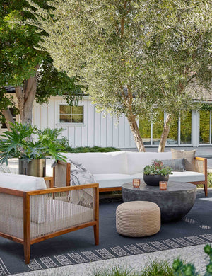 The Halia gray and white geometric throw blanket sits in an outdoor space underneath a white and woven sofa and accent chair, a woven pouf, and a metallic circular coffee table
