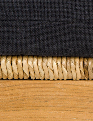 Close-up of the three textures on the Regine wooden accent chair: the black fabric, rattan detailing, and natural wooden frame